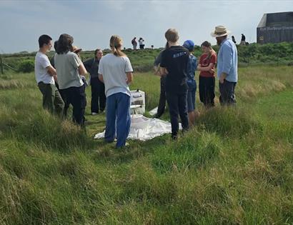 Teen Wildlife Rangers gathered in grassland at Rye Harbour Nature Reserve, taking part in an outdoor nature activity.