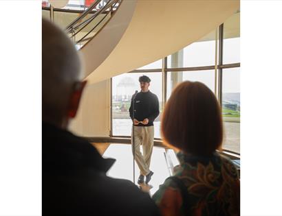 Exhibition tour at De La Warr Pavilion, with a speaker addressing visitors beside the pavilion’s curved window wall.