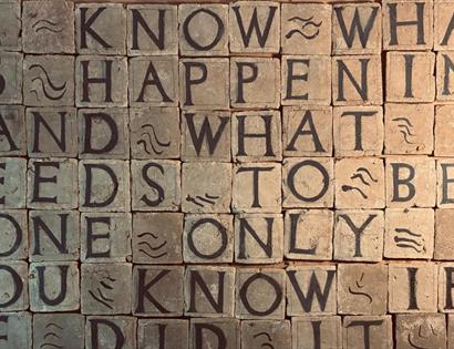 Wall of carved stone tiles displaying a bold text artwork featured in the new exhibition at BlackShed Gallery.
