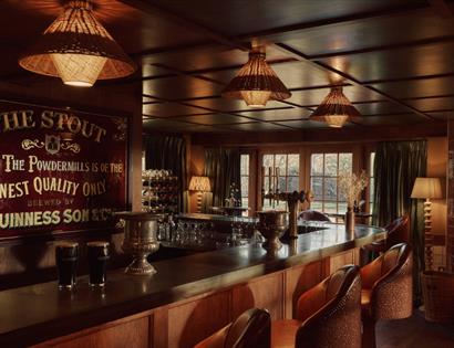 Cosy bar at Crafted at Powdermills with wooden counter, vintage sign, warm lighting and a lit fireplace.