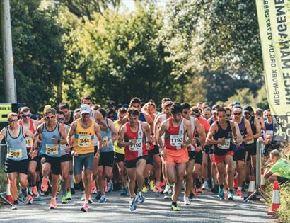 Photo of a Nice Work Race event. The photograph shows  lots of runners on the route of a race. They are all packed together and running on a road