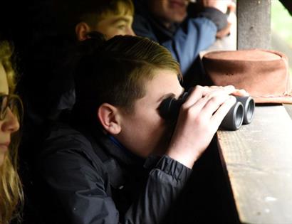 Children watching birds through binoculars at a hide in Rye Harbour Nature Reserve, focused on wildlife beyond the window.