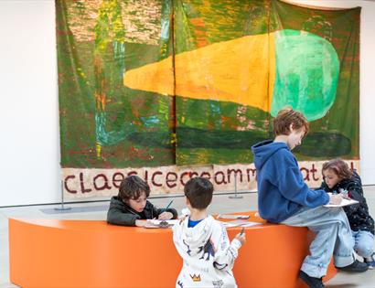 Children enjoying creative activities during a family day at Hastings Contemporary, seated in front of colourful artwork.
