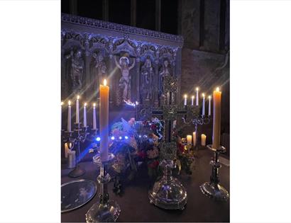 Image shows the Altar at St Thomas the Martyr Church with tall candles that are alight and an image of Jesus in the background on the cross.
