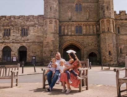 amily sitting on a bench outside a historic stone abbey building on a sunny day.