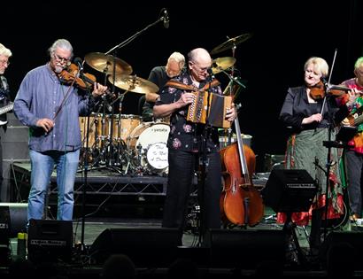 Photo of folk musicians on stage with string instruments.