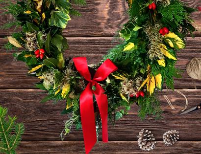 Image shows a christmas wreath decorated with bows, holly and pine cones
