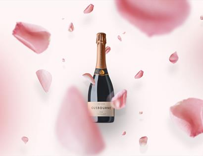 a bottle of gusbourne wine on a pink background with falling flower petals