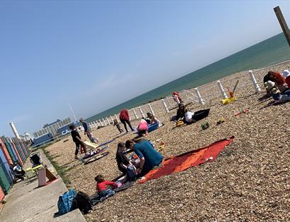 pebble beach with beach huts and people sitting on picnic blankets