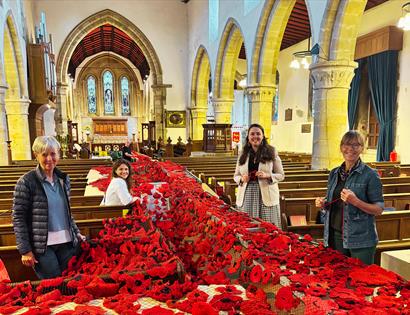 Image shows the inside of St Marys Church with the handmade poppys for the event. There are 4 members of the team standing with the poppys. 