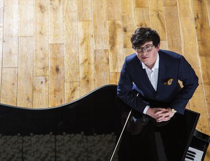 birds eye shot of man in suit stood with hands clasped on piano top