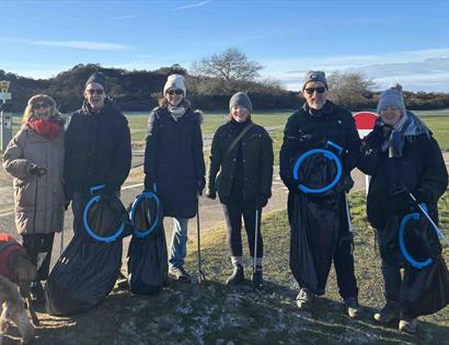 Volunteers at a community beach clean in Camber, standing outdoors with litter pickers and full rubbish bags on a sunny day.