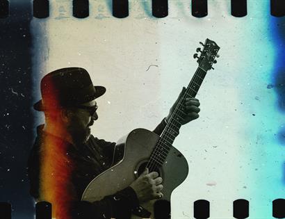 35mm film image with visible sprocket holes. Shows a man in a bowler hat playing guitar.