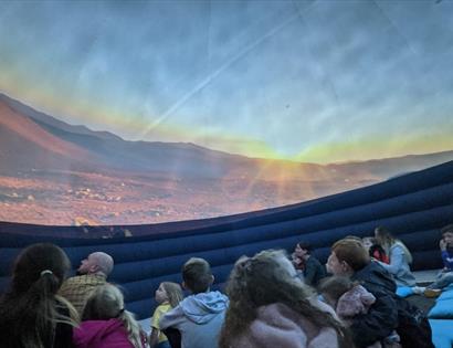 image shows the planetarium at Hastings museum. It also shows a picture of the sky with children and adults sitting and looking up.