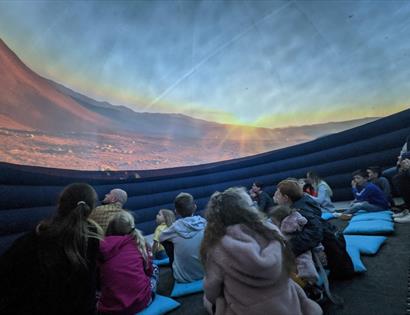 children stat inside a planetarium looking up a bare red planet landscape.