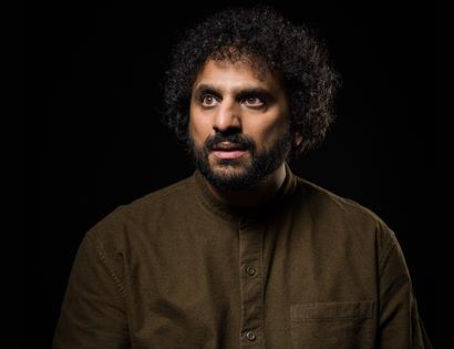 Nish Kumar on a black background wearing brown