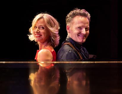 Photograph of Liza Pulman and Joe Stilgoe sat by a piano.