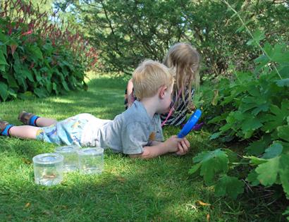 two young children exploring in a garden with pots and a magnifying glass.