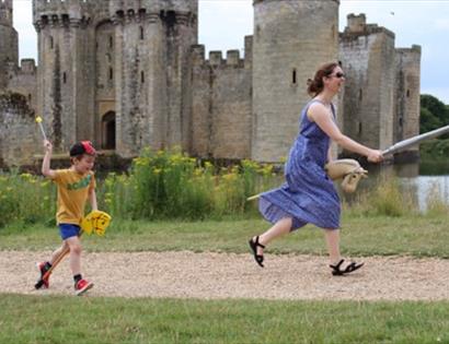 Summer of Play at Bodiam Castle, with visitors running on hobby horses beside the medieval castle and moat.