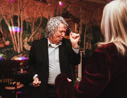 man with foil silver wig making shapes on the dancefloor.