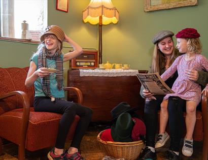 children and mum sat in 50s-style living room wearing hats.