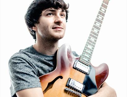 white man with dark hair hugging his guitar, white background