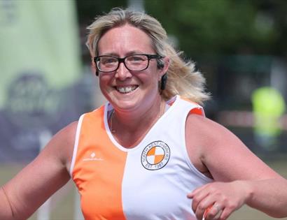 Runner in an orange and white athletic top holding a water bottle during an outdoor race.