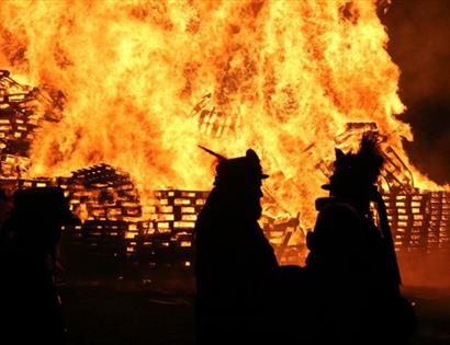 huge bonfire fire of pallet crates with two silhouetted figures in the foreground
