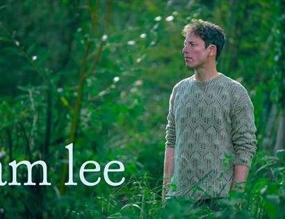 Image shows singer, Sam Lee, in a leafy, green outdoor environment with 'Sam Lee' written