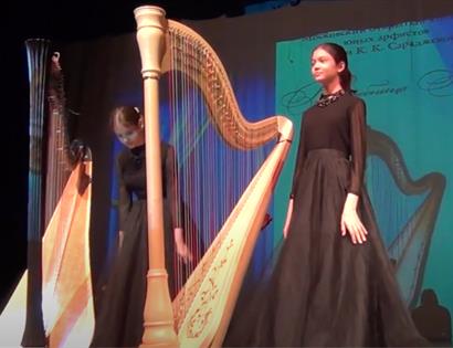 lady on stage in black dress stood next to harp.