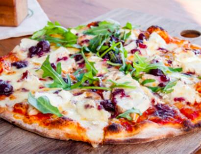 A photograph of a pizza topped with mozzarella and rocket, placed on a chopping board. For a pizza night event at the hub bodiam rother
