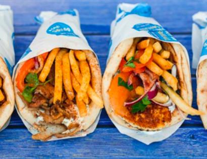 A photograph of four wrapped soulakis in a row, on a blue bench table. Photo for food event at the hub bodiam rother