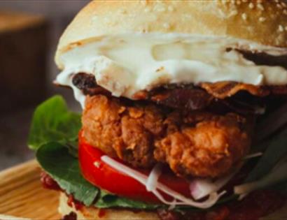 A close up of a stacked burger in a seeded bun, on a bamboo plate. To advertise The Pork Box event at The Hub, Bodiam, Rother.