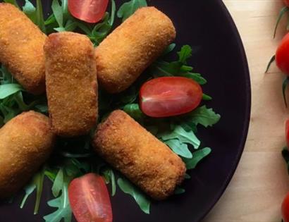 Tapas food, fried food arranged on a black plate with rocket leaves and tomatoes. For an event at The Hub, Bodiam, Rother.