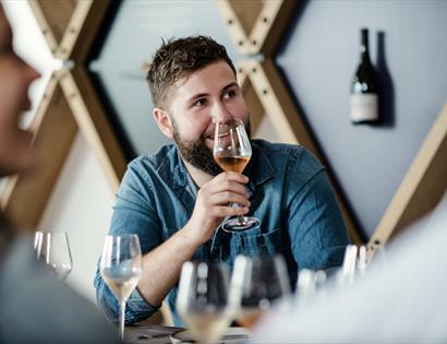 a white man with a raised wine glass, sat at a table.
