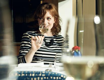 A lady smiling sipping white wine.