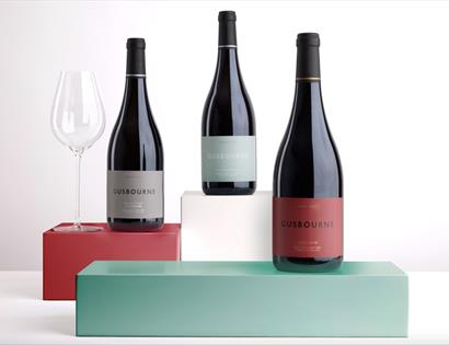 three wines bottles staggered on green, white and red box stands, against white background.