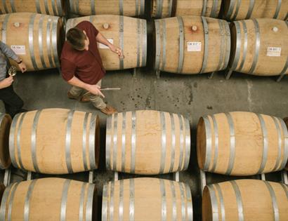 birds eye view of winery with two men walking past rows of barrels.