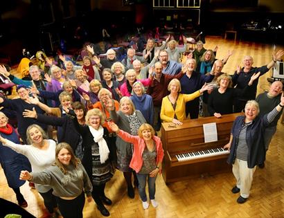photograph looking down onto stage with members large group around piano.