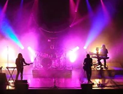 a photograph of think floyd on stage. Silhouette of band against bright pink, yellow and blue stage lights.