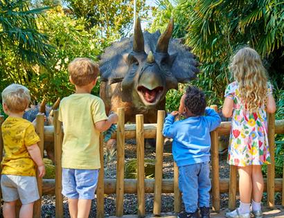 Children standing by a wooden fence looking at a large dinosaur model at Drusillas Park.