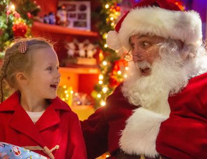 A young girl and Father Christmas look at each other engaged in conversation.