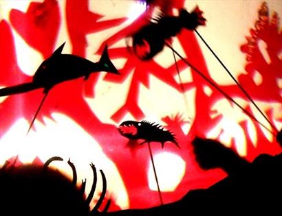 shadow puppets of underwater creatures against a red and white background.