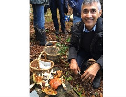 man crouching next to basket and foraged mushrooms.
