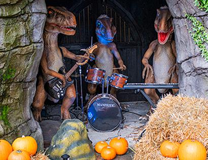 Halloween at Knockhatch Adventure Park featuring animatronic dinosaurs playing instruments among pumpkins and hay bales.