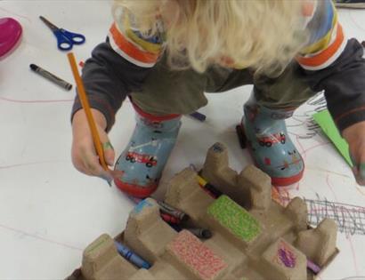 small blond boy in wellies standing on doodled paper with pencil in hand.