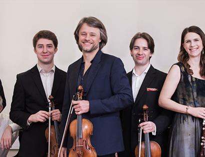 a long group portrait of musicians holding instruments, all white and wearing smart dress. All men except for one woman in silver dress.