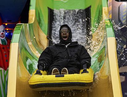 Visitor riding a water slide past Halloween characters during Half Term Horrors at Knockhatch Adventure Park.