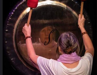 woman banging a gong face reflected in it