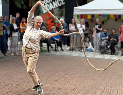 Outdoor performance by JUTE at De La Warr Pavilion, showing an older dancer swinging a rope as an audience watches.